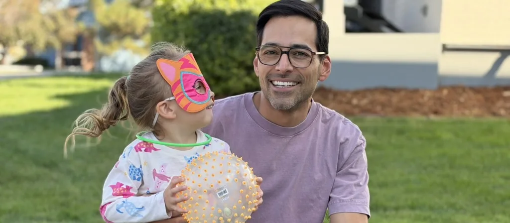 Ricardo outdoors with his daughter, who is wearing a cat mask